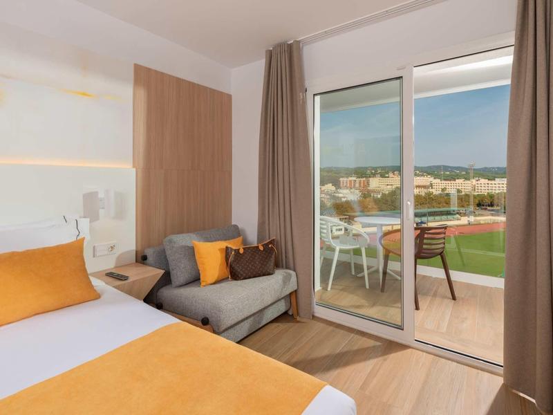 Camera d'hotel moderna con letto matrimoniale, divano grigio e balcone con vista mare.