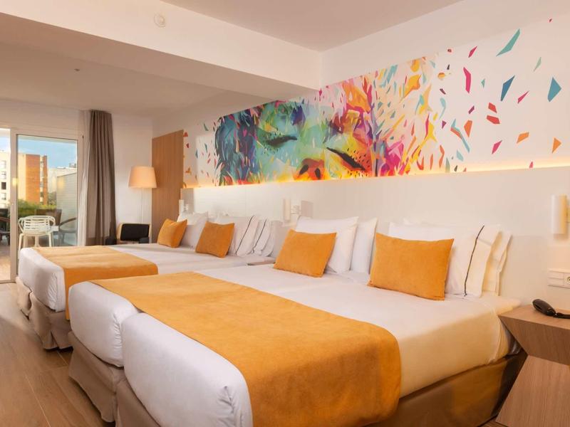 Camera d'albergo con due letti grandi, cuscini arancioni e un murale colorato.