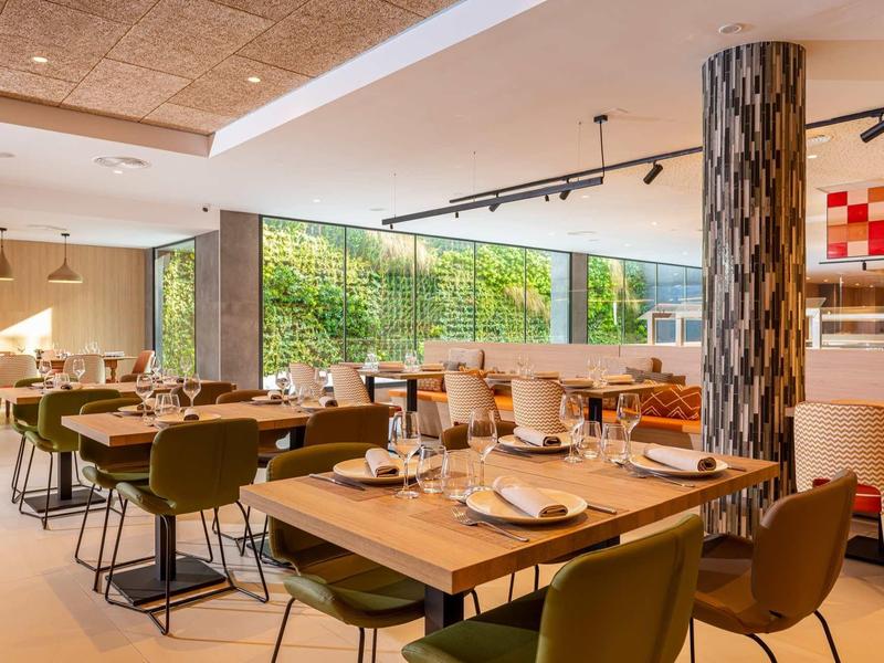 Ristorante moderno con accenti in legno e verde, tavoli apparecchiati e parete vegetale verticale.