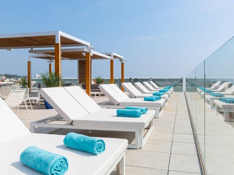 Terrazza sul tetto soleggiata con lettini e asciugamani blu vicino a una barriera in vetro con vista mare.