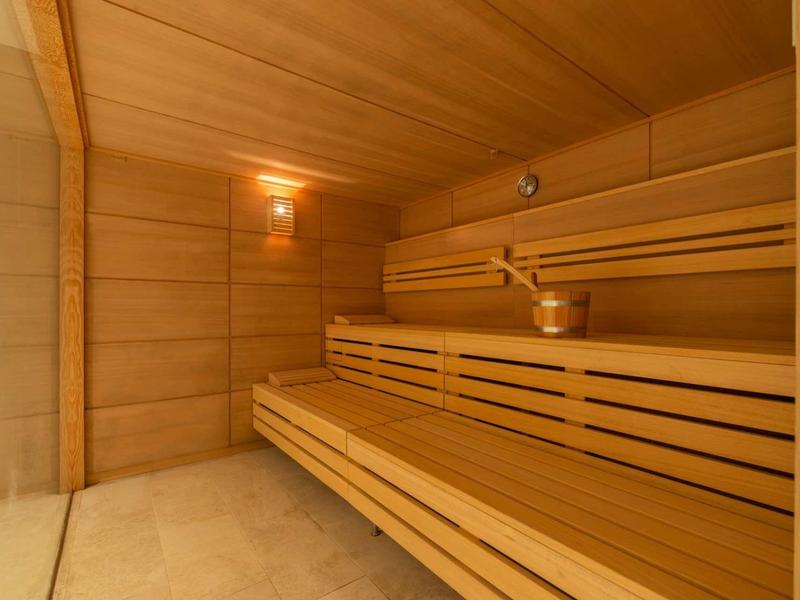 Sauna in legno chiaro con illuminazione soffusa e accessori tradizionali.