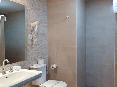 Moderní hotelová koupelna se dřezem, toaletou a sprchovým koutem v neutrálních odstínech.