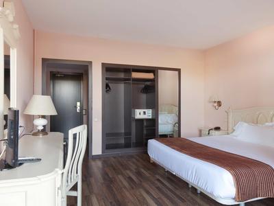 Světý hotelový pokoj s manželskou postelí, psacím stolem, židlí a moderním zařízením.