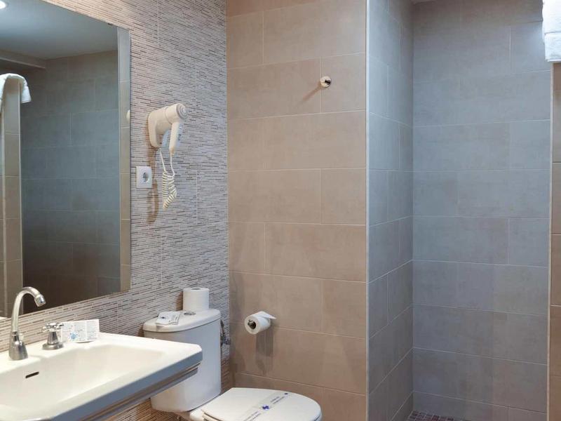 Moderní hotelová koupelna se dřezem, toaletou a sprchovým koutem v neutrálních odstínech.