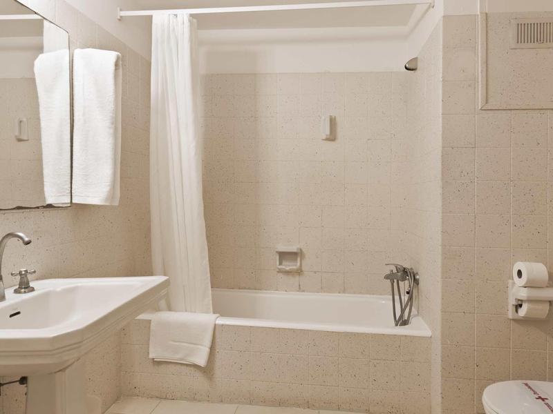 Jasně zařízená hotelová koupelna s vanou, umyvadlem a ručníky.