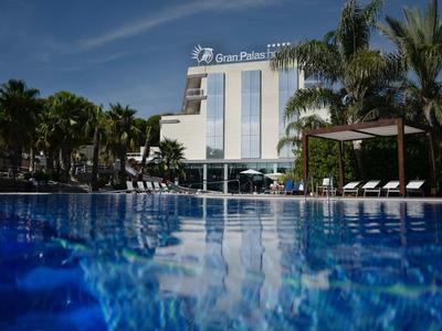 Luxurious hotel with pool, palm trees, and lounge chairs under sunny sky.