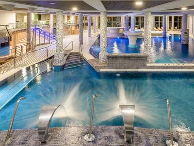 Indoor hotel pool area with clear water, lounge chairs, and ambient lighting.