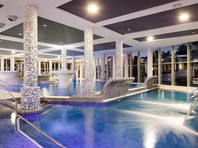 Indoor luxury pool with water features and comfortable lounge chairs at night.