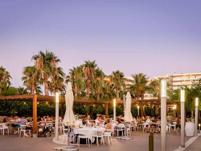 Ristorante all'aperto con tavoli, sedie e palme al tramonto.