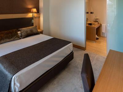 Modern hotel room with large bed, nightstand, lamps, and a desk with chair.