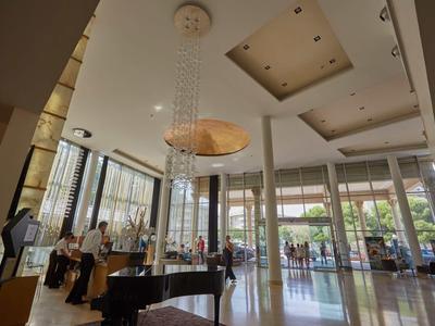 Spacious hotel lobby with a grand piano, modern chandelier, and large windows letting in natural light.