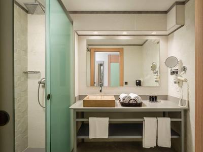 Modern hotel bathroom with glass shower, large mirror, stone sink, and neatly folded towels.
