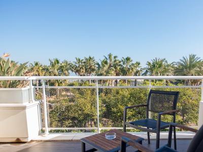 Balcony with chairs and table overlooking palm trees against a clear blue sky.