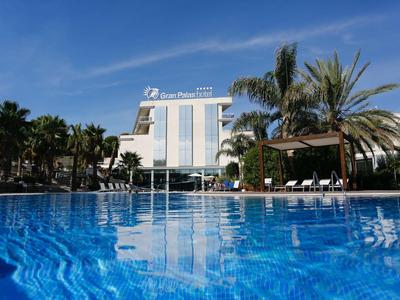 Complesso alberghiero moderno con grande piscina blu e palme sotto un cielo sereno.