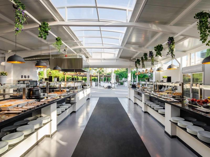 Bright, spacious buffet area with white counters, hanging plants, and a skylight ceiling.