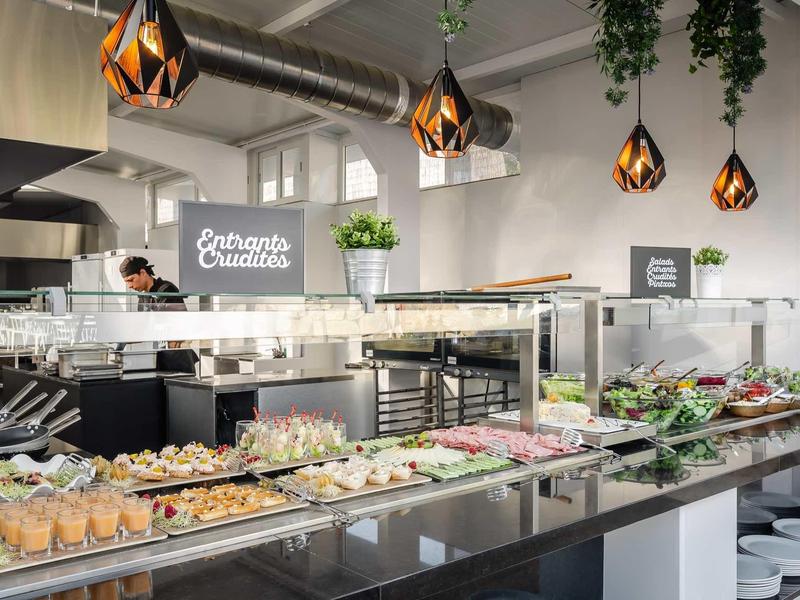 Modern buffet setup with assorted sandwiches, salads, and hanging pendant lights in a bright dining area.