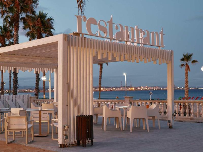 Outdoor restaurant terrace with tables and chairs by the sea during evening.