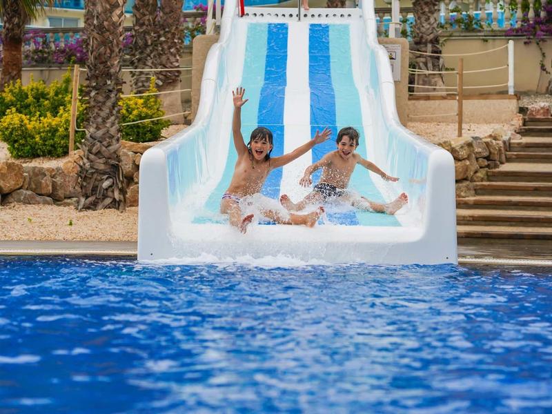 Two people sliding down a blue and white water slide into a pool.