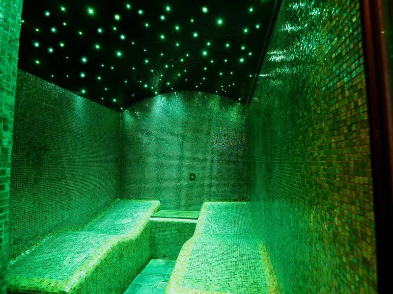 Indoor spa room with green mosaic benches and starry ceiling lights.