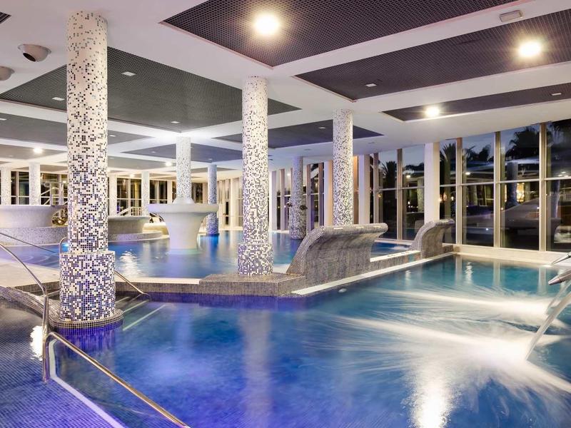 Indoor luxury pool with water features and comfortable lounge chairs at night.
