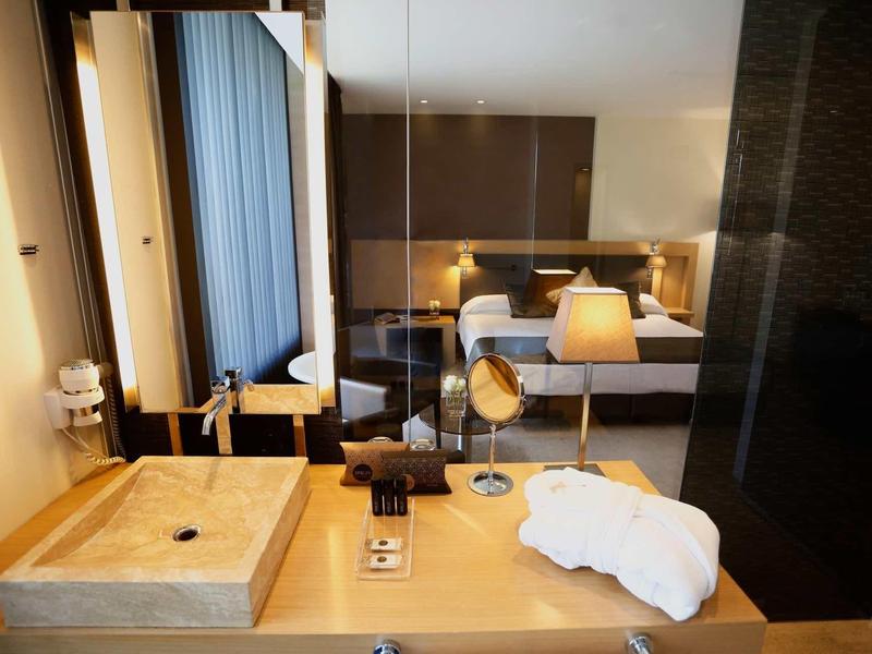Modern hotel room with bed, bedside lamps, large mirror, and a sink countertop.