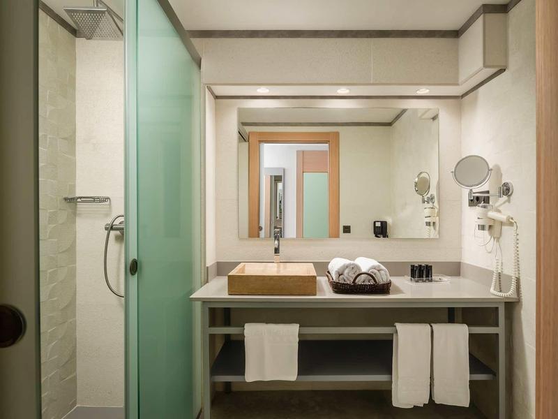 Modern hotel bathroom with glass shower, large mirror, stone sink, and neatly folded towels.