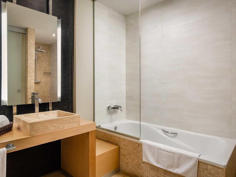Modern hotel bathroom with wooden sink, large mirror, and bathtub with towel.