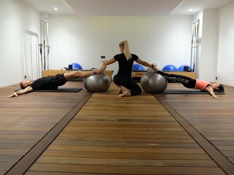Three people stretching with exercise balls in a well-lit room with wooden floors.