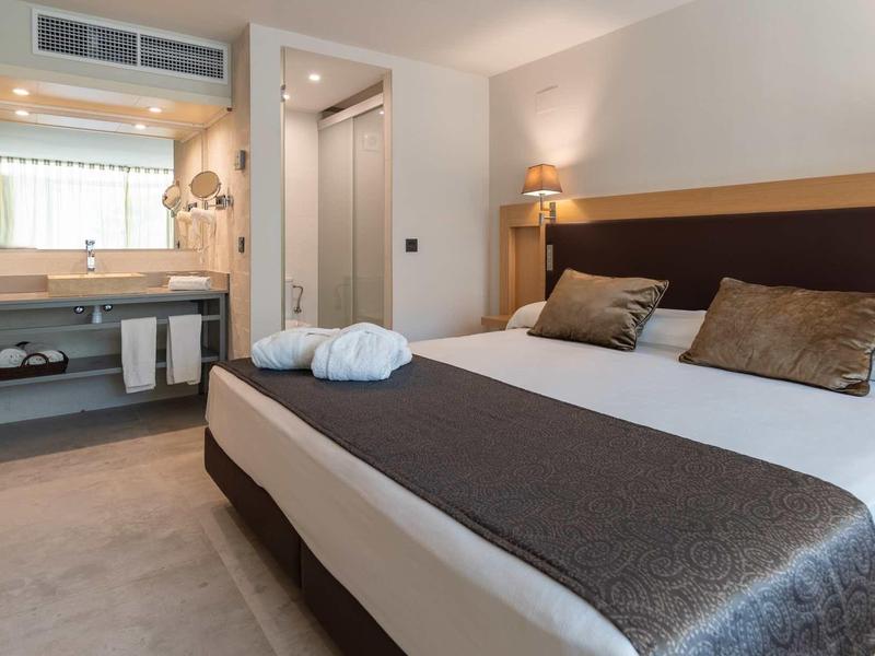 Modern hotel room with a large bed, bedside lamp, and an open view of the bathroom vanity.