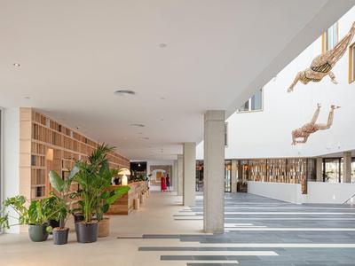 Ampia hall d'hotel moderna con piante, scaffali in legno e decorazioni sospese di rami.