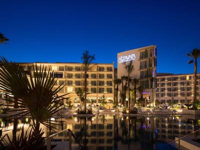 Verlicht hotel met palmbomen en waterreflectie 's nachts.