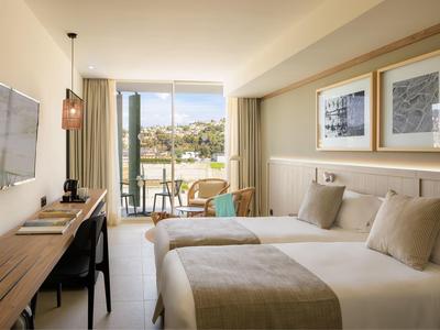 Camera d'hotel moderna con due letti, scrivania, TV e balcone con posti a sedere all'aperto.