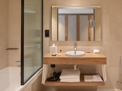 Bagno moderno con mobile in legno, lavabo rotondo, grande specchio, vasca da bagno e WC.