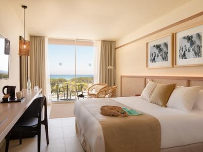 Camera d'hotel luminosa con grande letto, due poltrone vicino alla finestra e vista mare.