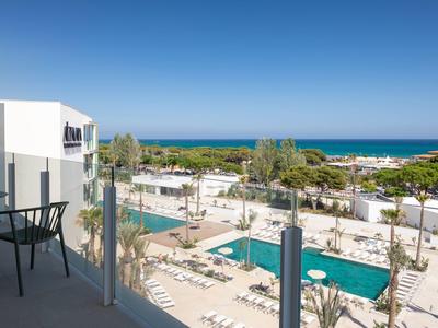 Vista dal balcone sulla piscina, lettini e mare sotto un cielo limpido.