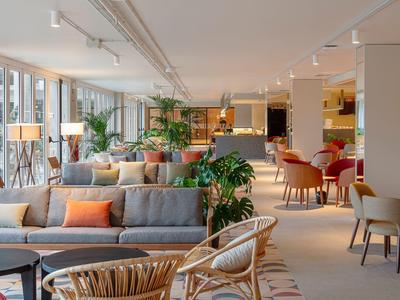 Ampio salone dell'hotel con divani moderni, sedie, piante e illuminazione calda.