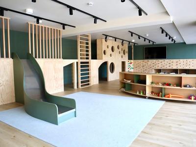 Area giochi interna moderna con scivolo, scaffali e strutture di arrampicata in legno.