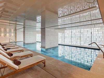 Piscina interna moderna con lettini e luce naturale attraverso grandi pareti di vetro.