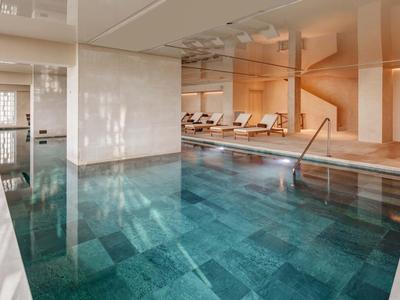 Piscina interna con acqua turchese limpida, sdraio e illuminazione calda per un'atmosfera rilassante.