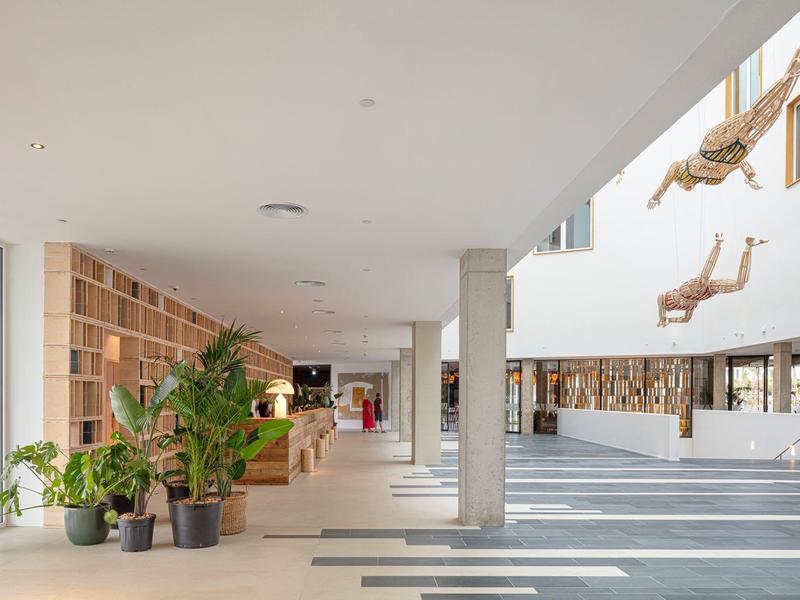 Ampia hall d'hotel moderna con piante, scaffali in legno e decorazioni sospese di rami.