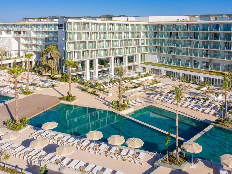 Hotel moderno con ampia area piscina e molte sdraio e ombrelloni.