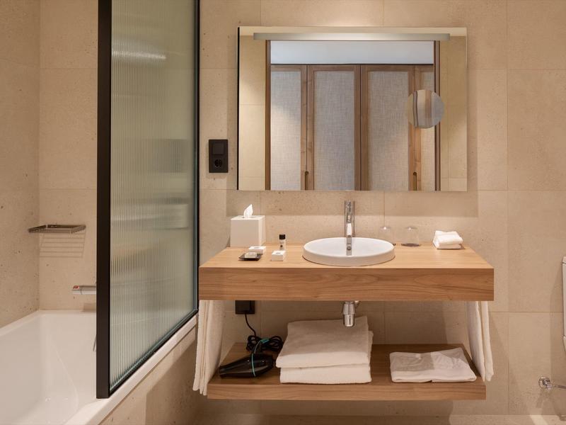 Bagno moderno con mobile in legno, lavabo rotondo, grande specchio, vasca da bagno e WC.