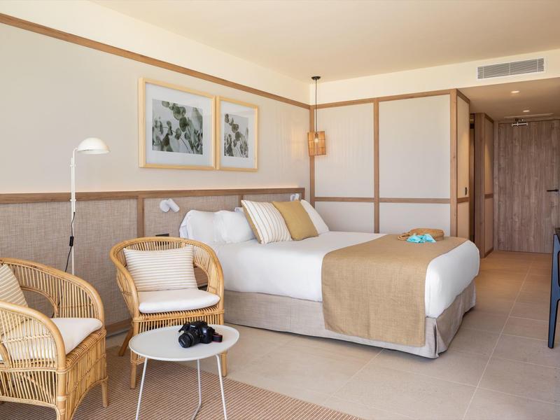 Camera d'hotel accogliente con letto matrimoniale, sedie in vimini, tavolino e decorazioni neutre.