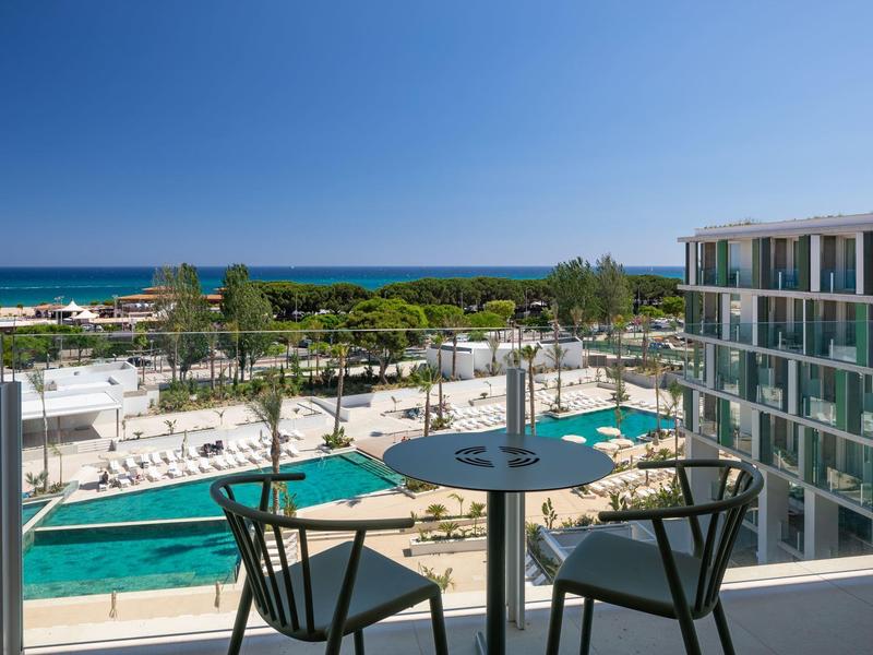 Vista dal balcone con tavolo, sedie, piscina, palme e oceano in lontananza