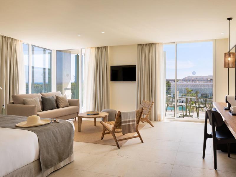 Camera d'hotel luminosa con letto, area salotto, balcone e vista sulla città.