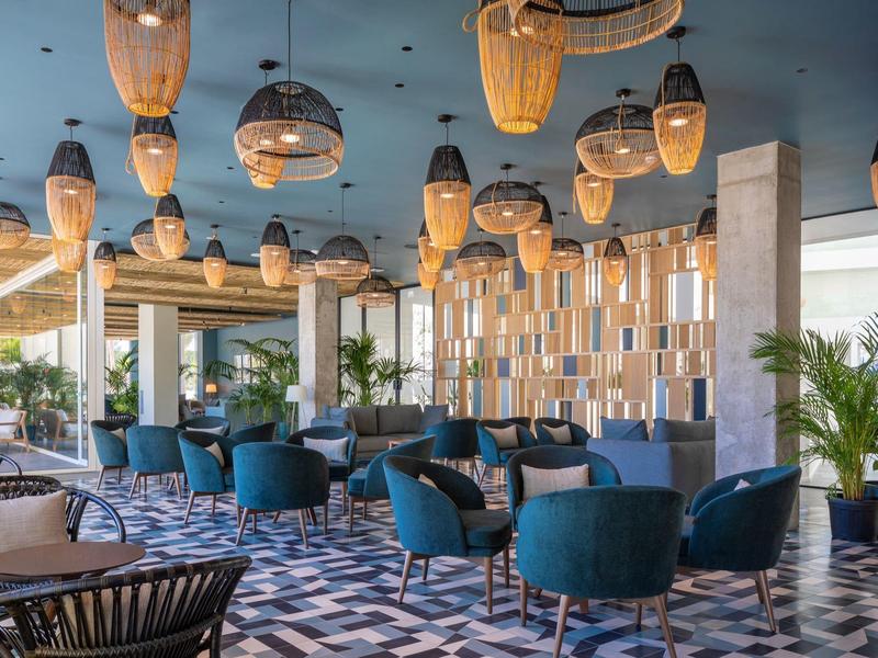 Lounge moderno in hotel con poltrone blu, pavimento decorato e lampade di vimini sospese.