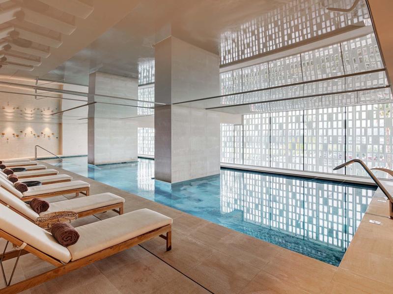 Piscina interna moderna con lettini e luce naturale attraverso grandi pareti di vetro.