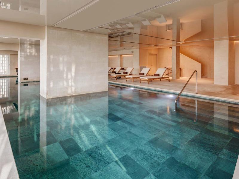 Piscina interna con acqua turchese limpida, sdraio e illuminazione calda per un'atmosfera rilassante.