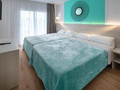 Moderna habitación de hotel con cama doble, acento de pared turquesa y suelo de madera clara.