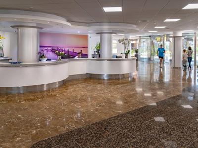 Amplia zona de vestíbulo de hotel con recepción curva, suelo de mármol e iluminación moderna.